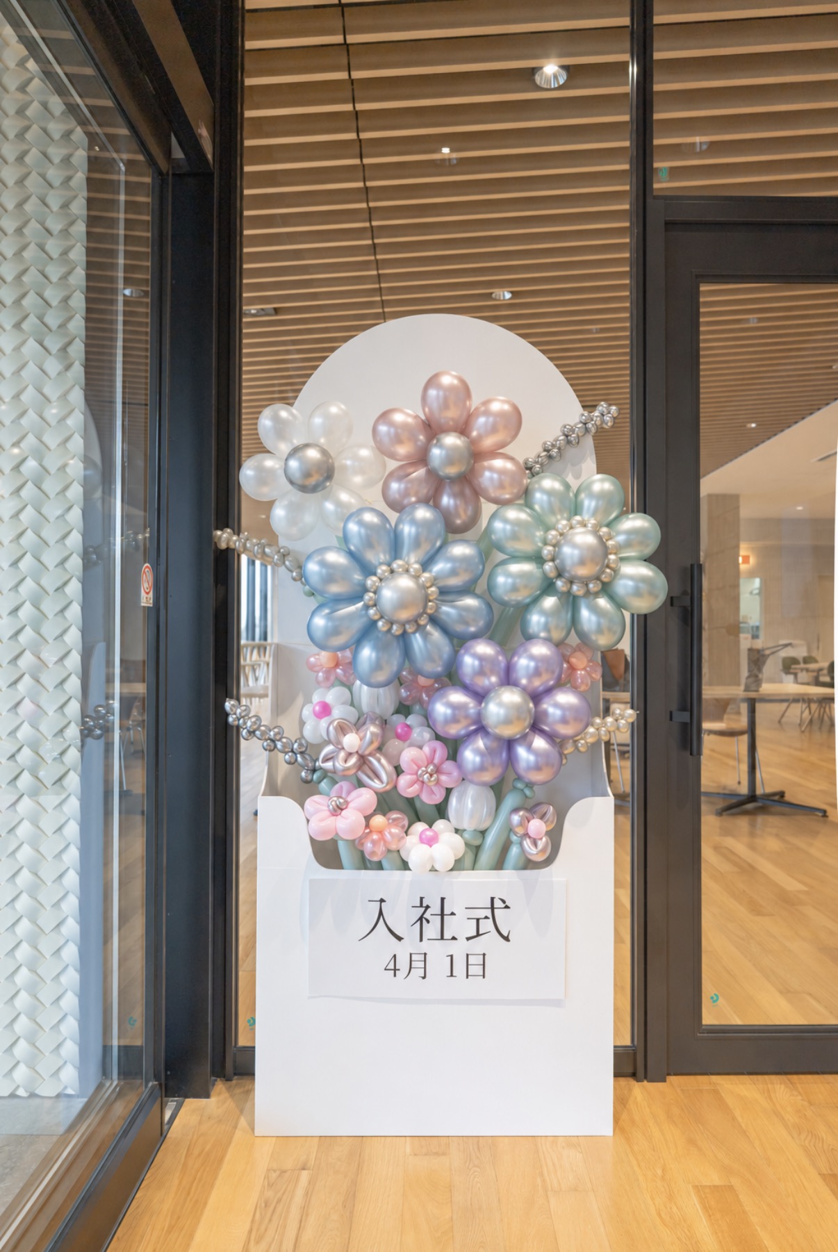 ガラスの入口の横に置いた、花の形のバルーンを飾った白いパネル